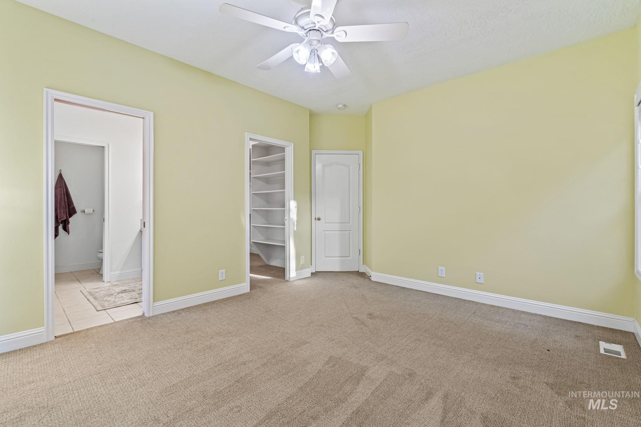 6099 North Heathrow Way Boise, ID 83713 - Photo 15 of 39 Unfurnished bedroom featuring light colored carpet, a spacious closet, a ceiling fan, light tile patterned floors, and connected bathroom