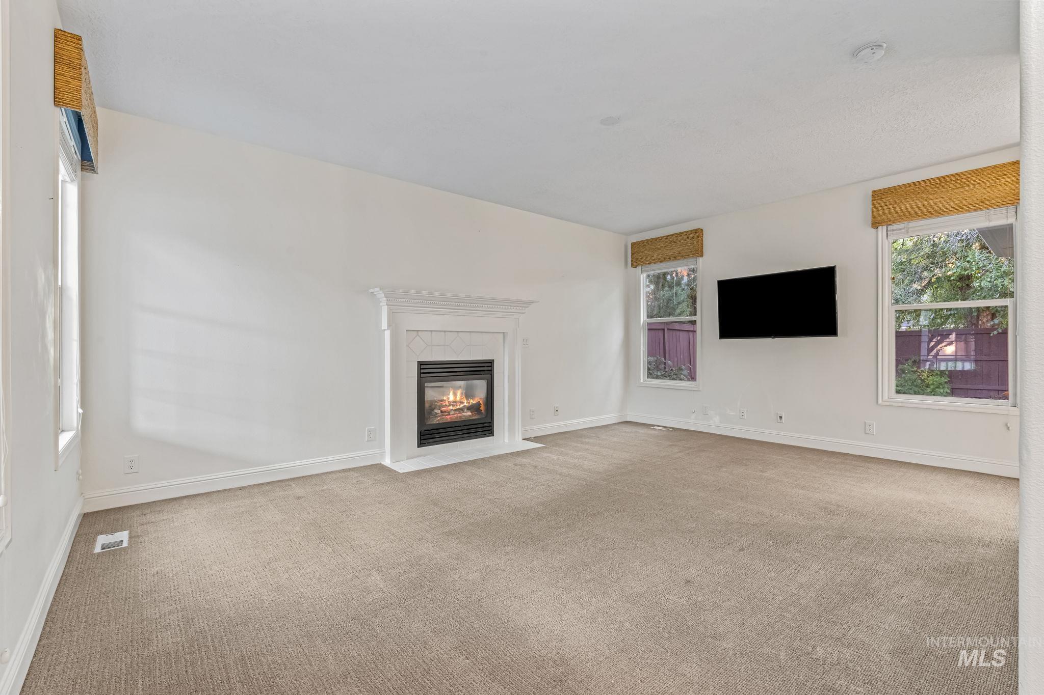 6099 North Heathrow Way Boise, ID 83713 - Photo 7 of 39 Unfurnished living room featuring carpet flooring, plenty of natural light, and a fireplace with flush hearth