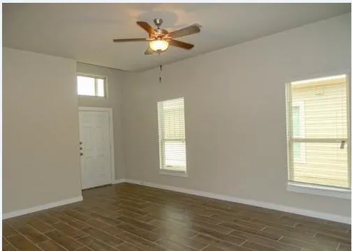 an empty room with wooden floor ceiling fan and windows