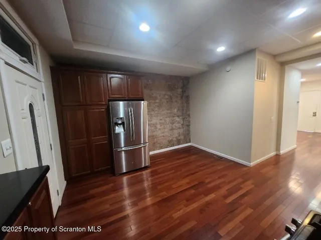 a view of a refrigerator in kitchen and an empty room with wooden floor windows