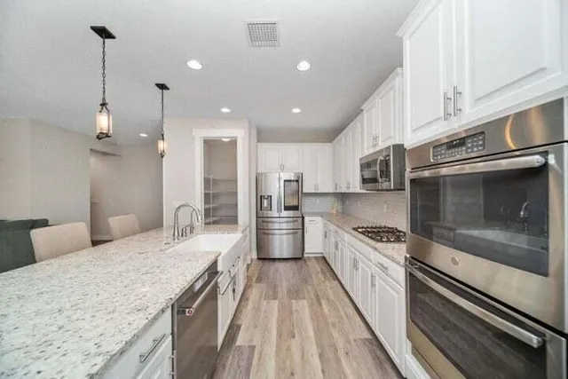 a large kitchen with stainless steel appliances kitchen island a large stove a oven a sink dishwasher and white cabinets with wooden floor