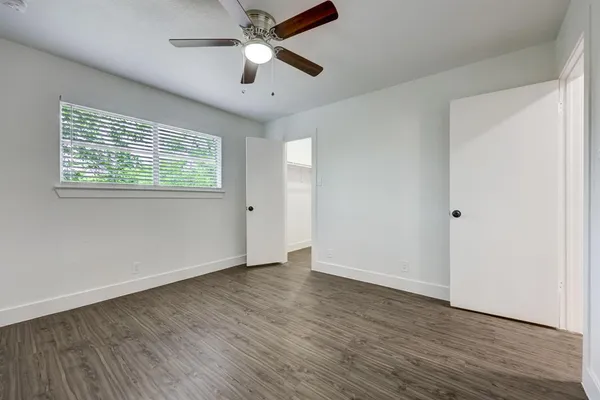 an empty room with wooden floor chandelier fan and windows