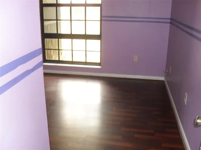 an empty room with wooden floor and windows with curtains