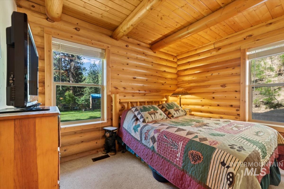 10 Elk Point Road Garden Valley, ID 83622 - Photo 20 of 42 Bedroom featuring rustic walls, light colored carpet, a wooden ceiling with exposed beams, and multiple windows