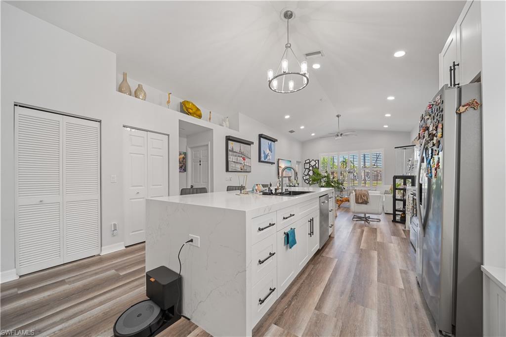 1638 Triangle Palm Terrace Naples, FL 34119 - Photo 5 of 21 Kitchen with vaulted ceiling, stainless steel appliances, light wood-type flooring, white cabinets, and an island with sink