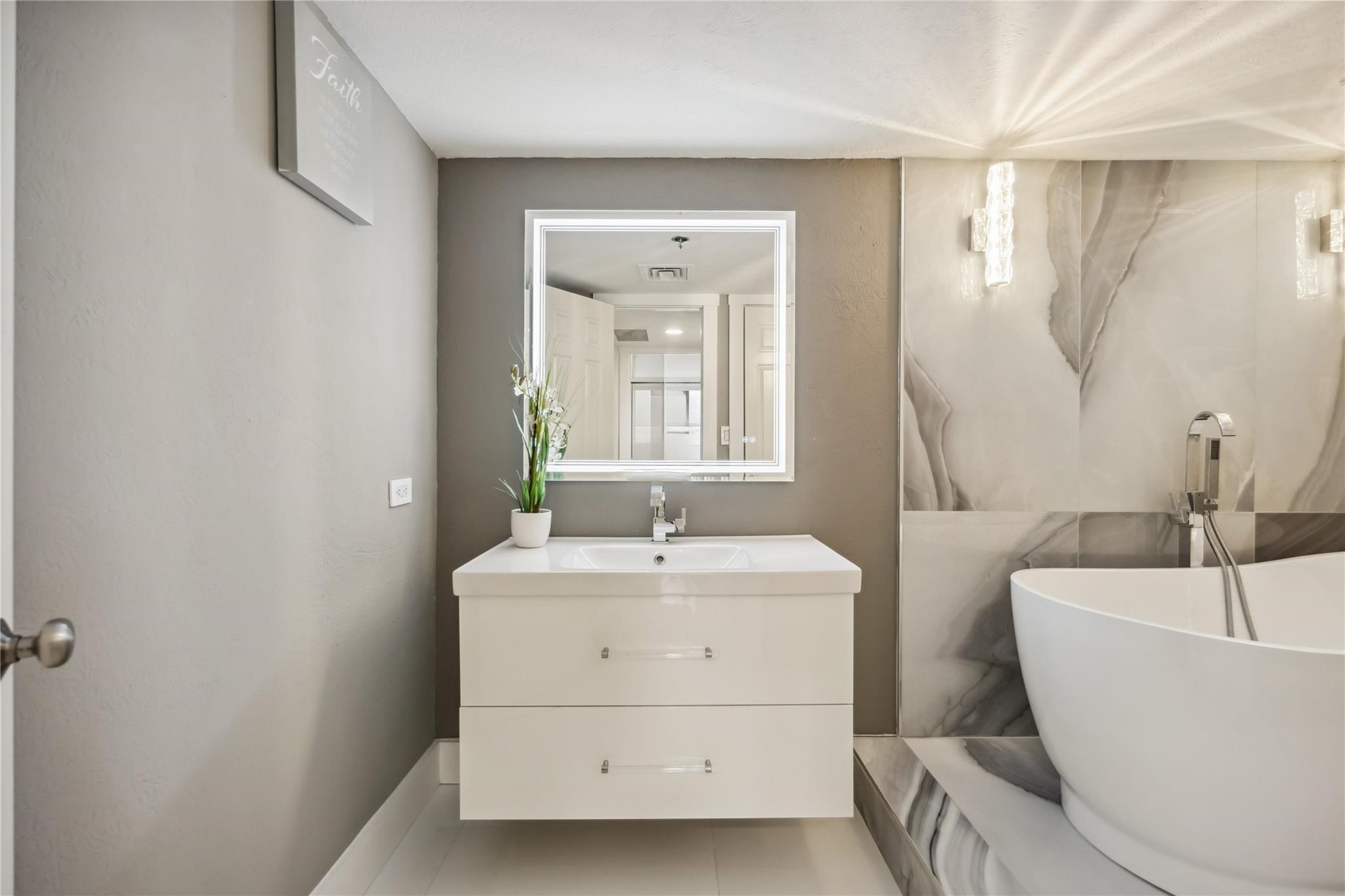 3525 Sage Road, Unit 1713 Houston, TX 77056 - Photo 18 of 25 Spa-inspired bathroom featuring a floating vanity, backlit mirror, and a luxurious soaking tub set on a marble pedestal—pure elegance.