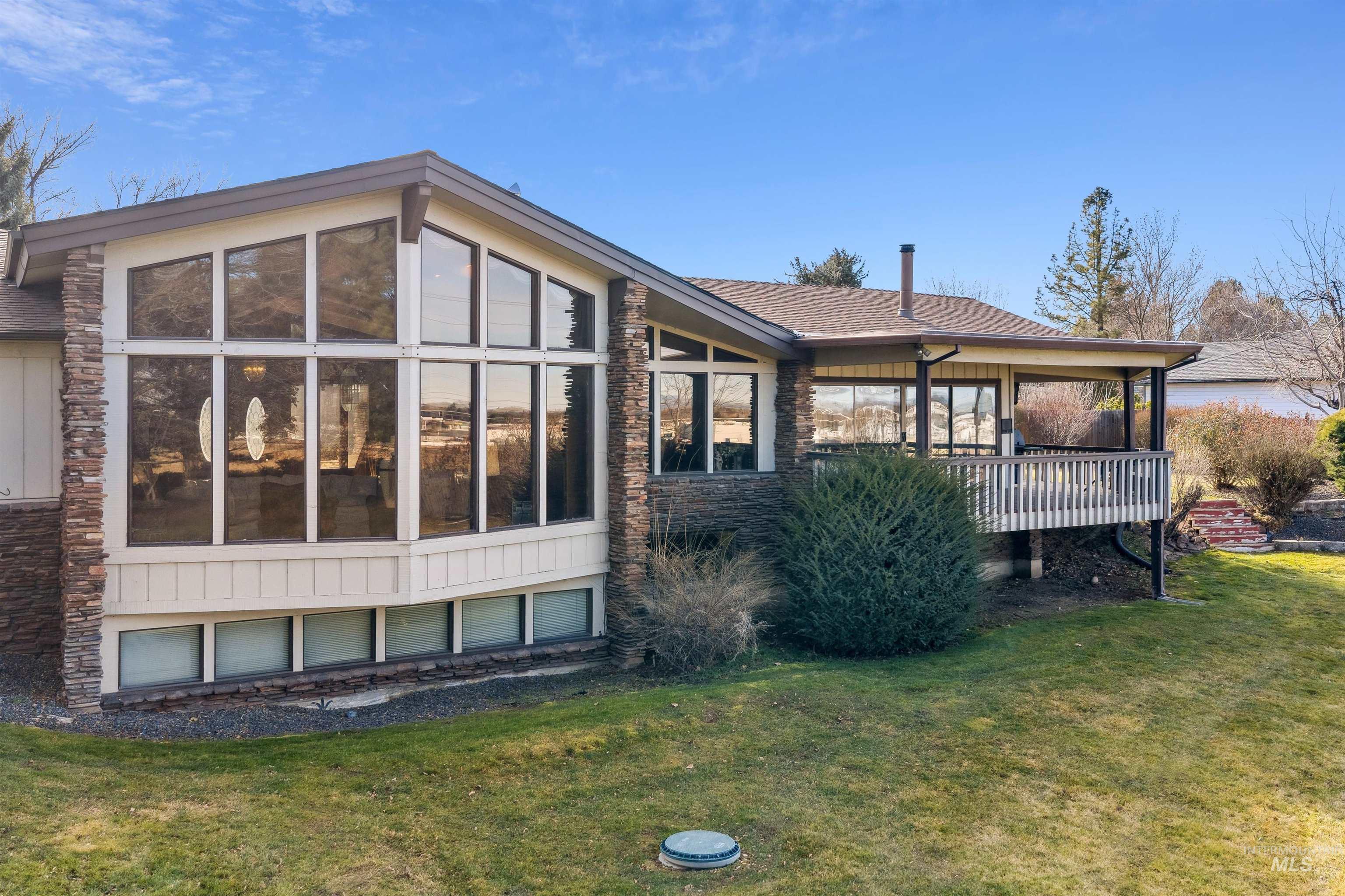10030 West Stardust Drive Boise, ID 83709 - Photo 4 of 50 Rear view of property with stone siding, a sunroom, a yard, and roof with shingles