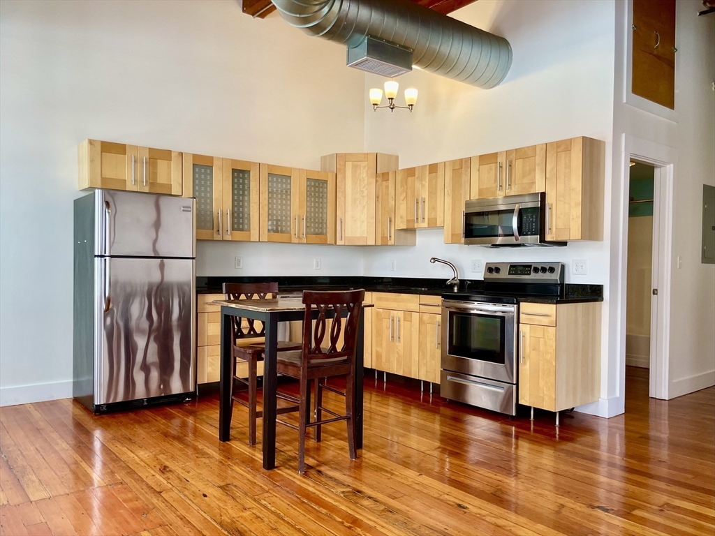49 Munroe Street, Unit 201 Lynn, MA 01901 - Photo 8 of 14 a kitchen with stainless steel appliances granite countertop a stove top oven a sink a dining table and chairs with wooden floor
