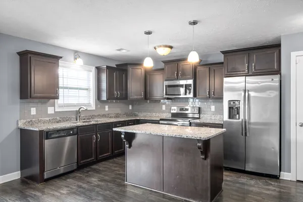 a kitchen with stainless steel appliances granite countertop a sink a stove a refrigerator cabinets and a center island