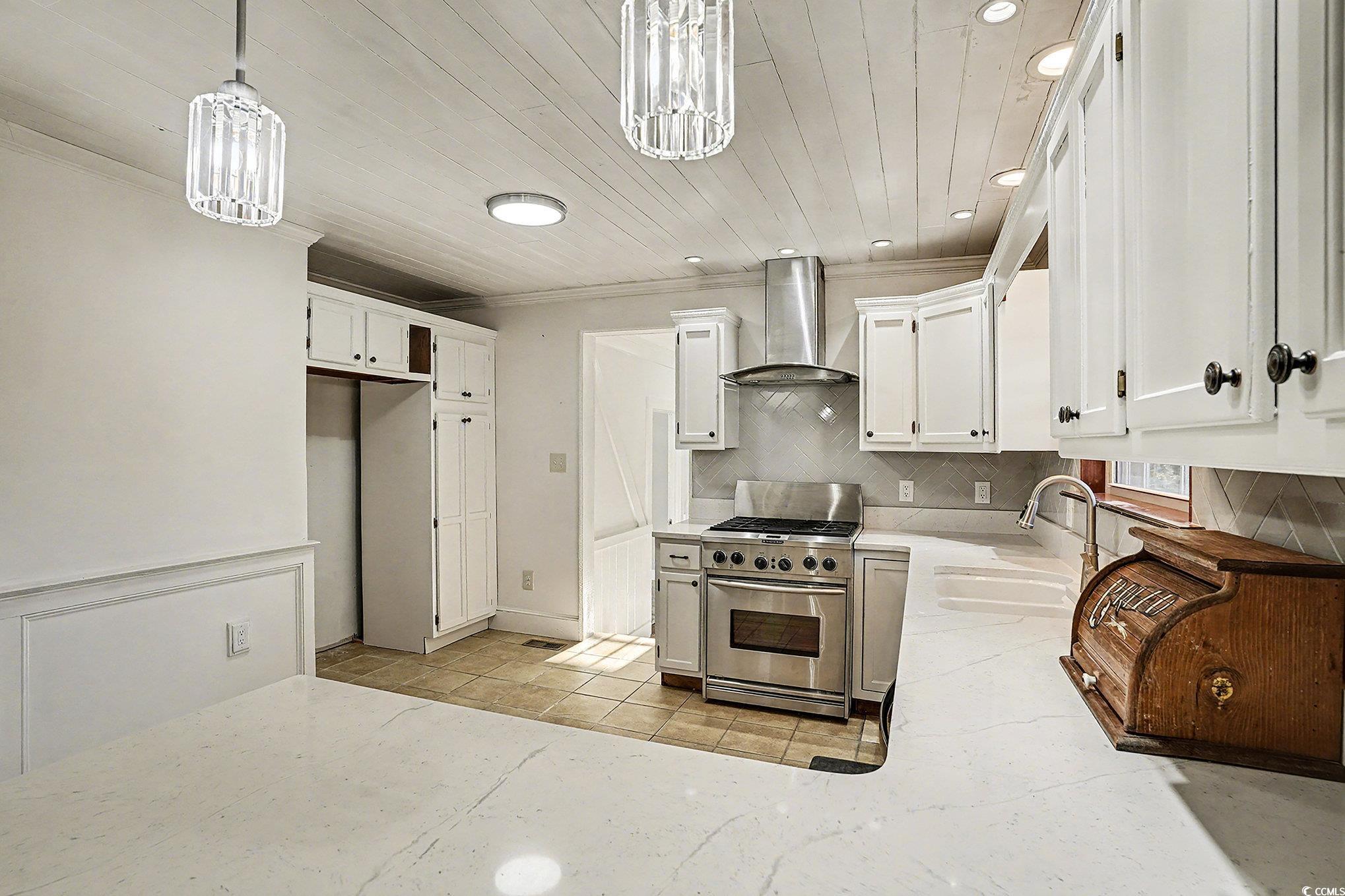 218 Busbee Street Conway, SC 29526 - Photo 12 of 30 Kitchen featuring white cabinetry, stainless steel gas stove, backsplash, wall chimney exhaust hood, and hanging light fixtures