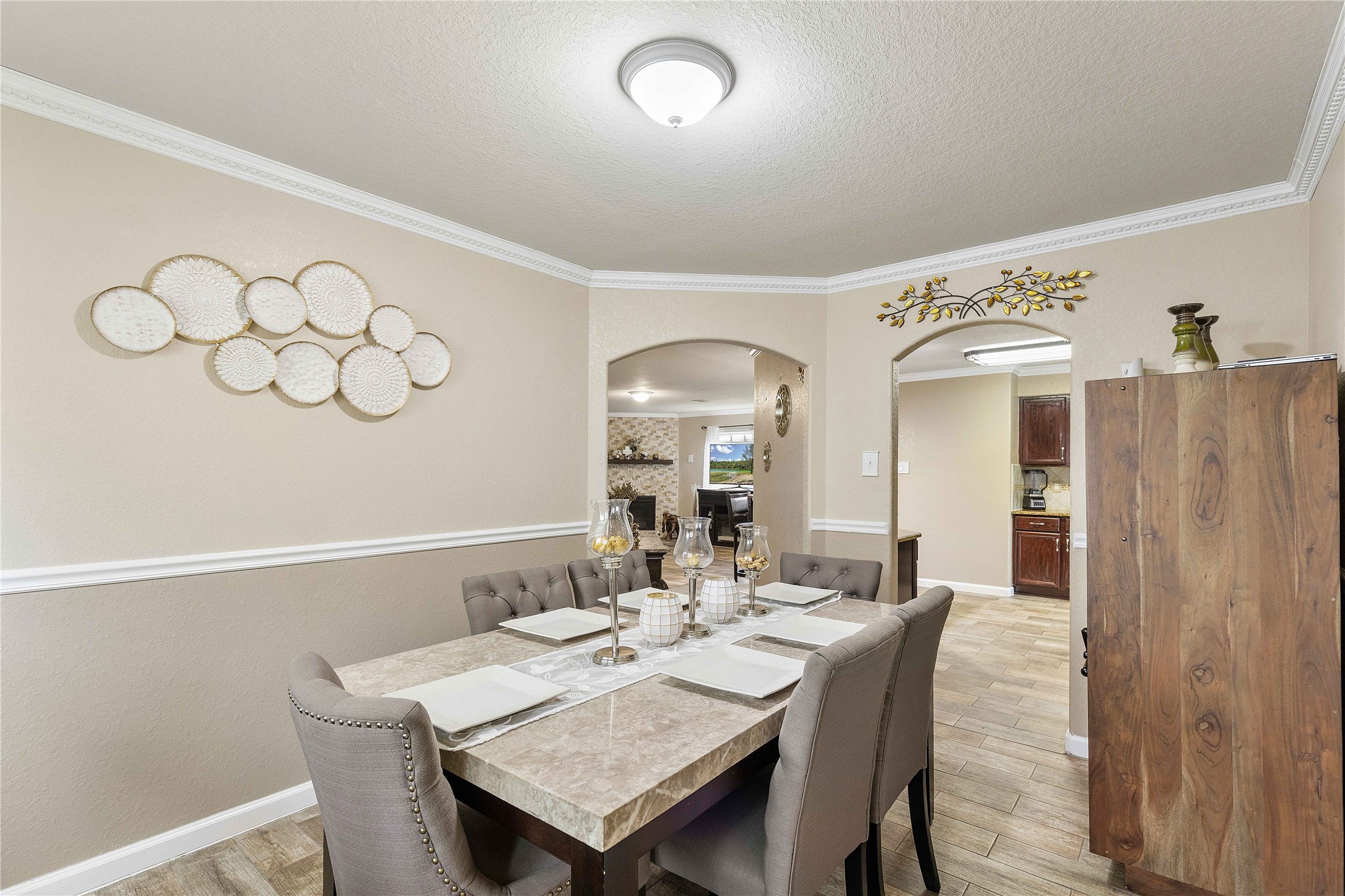 11031 Bauer Elm Street Houston, TX 77044 - Photo 16 of 33 This elegant dining room features a modern table set for six, neutral walls with decorative accents, and stylish crown molding. It opens seamlessly into the living area and kitchen through graceful archways, offering a warm and inviting atmosphere.