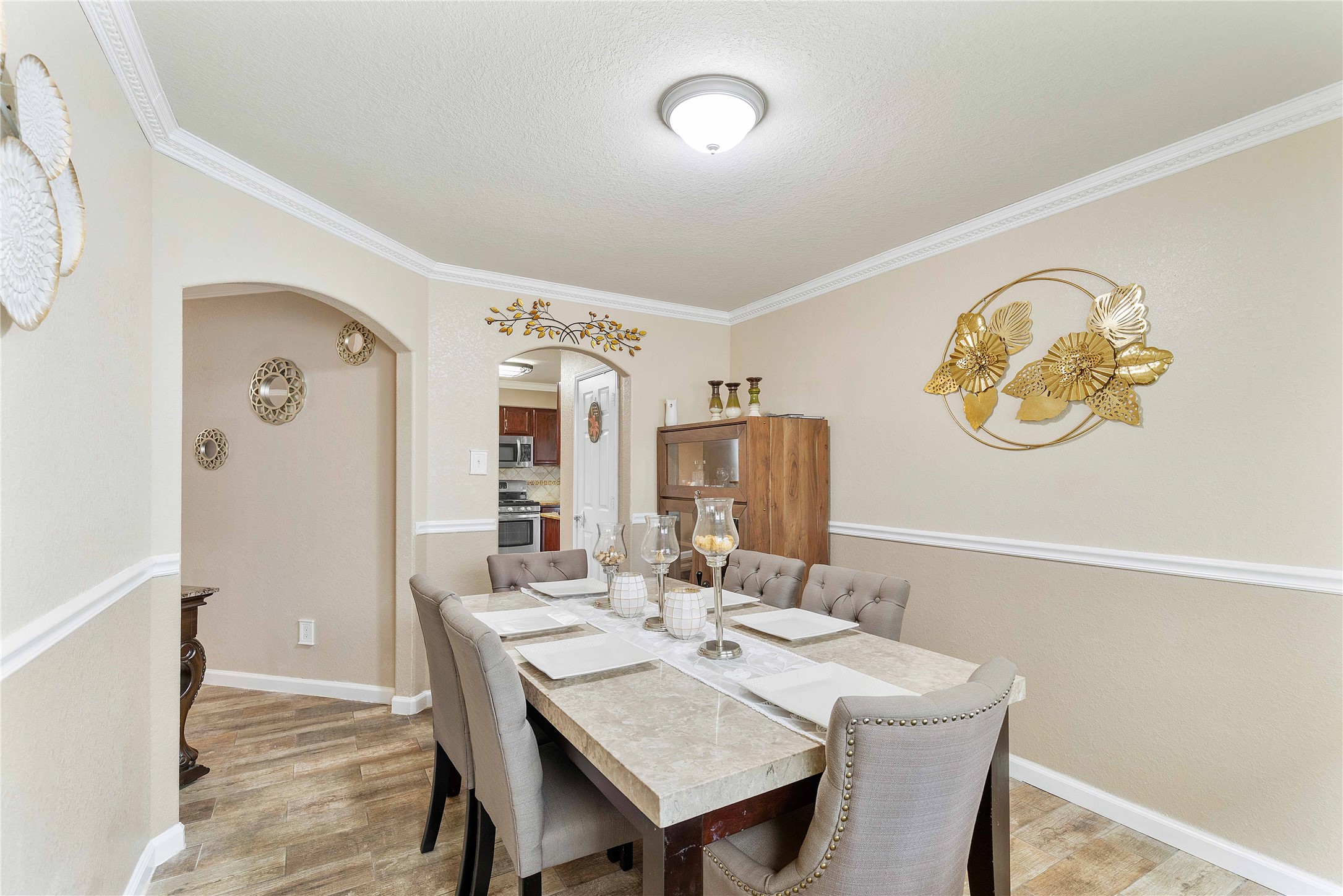 11031 Bauer Elm Street Houston, TX 77044 - Photo 17 of 33 This dining room features a cozy layout with elegant decor, including gold wall art and a stylish light fixture. The room has neutral tones, a marble-topped table, and cushioned chairs, creating an inviting atmosphere. An arched doorway leads to the kitchen, enhancing the home's flow.