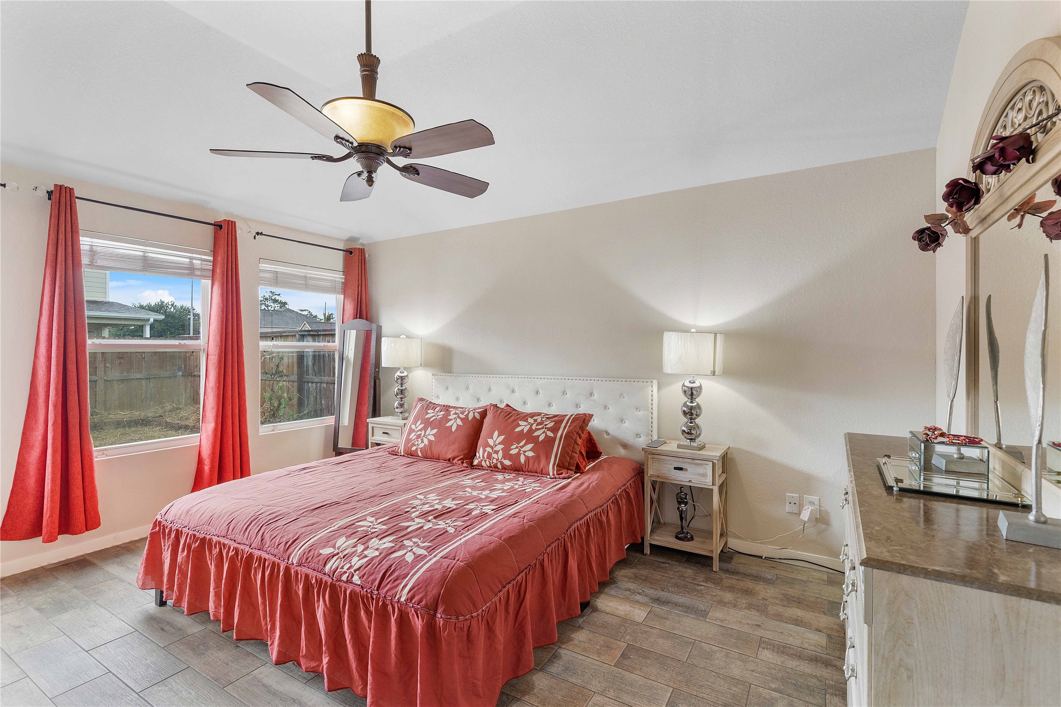 11031 Bauer Elm Street Houston, TX 77044 - Photo 24 of 33 Bright bedroom with large windows, red curtains, and a comfortable bed with matching linens. Features a ceiling fan, elegant nightstands, and tasteful decor.