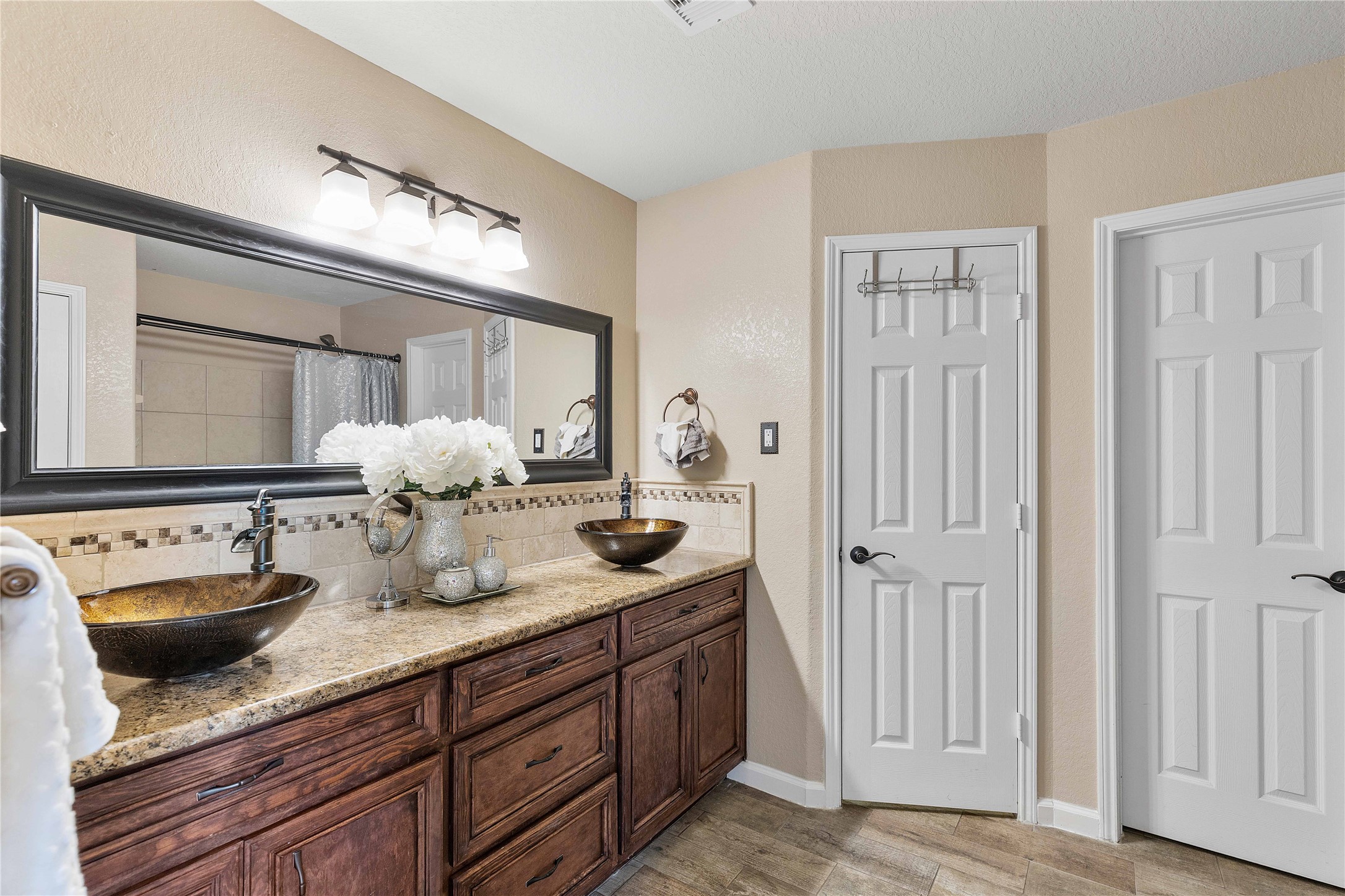 11031 Bauer Elm Street Houston, TX 77044 - Photo 27 of 33 This bathroom features a spacious double vanity with elegant vessel sinks and a granite countertop. The large mirror and modern light fixture add brightness, while the neutral tones and wood cabinetry create a warm, inviting atmosphere.