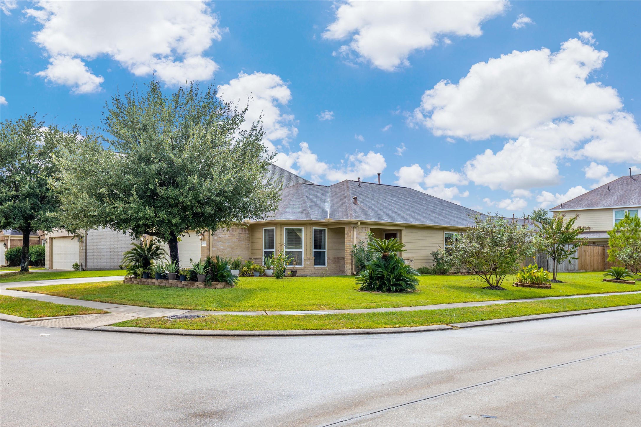 11031 Bauer Elm Street Houston, TX 77044 - Photo 4 of 33 This photo showcases a charming single-story home on a corner lot, featuring a well-maintained lawn and mature trees. The house has a neutral exterior with a mix of brick and siding, and large windows provide ample natural light. The neighborhood appears peaceful with clear skies above.