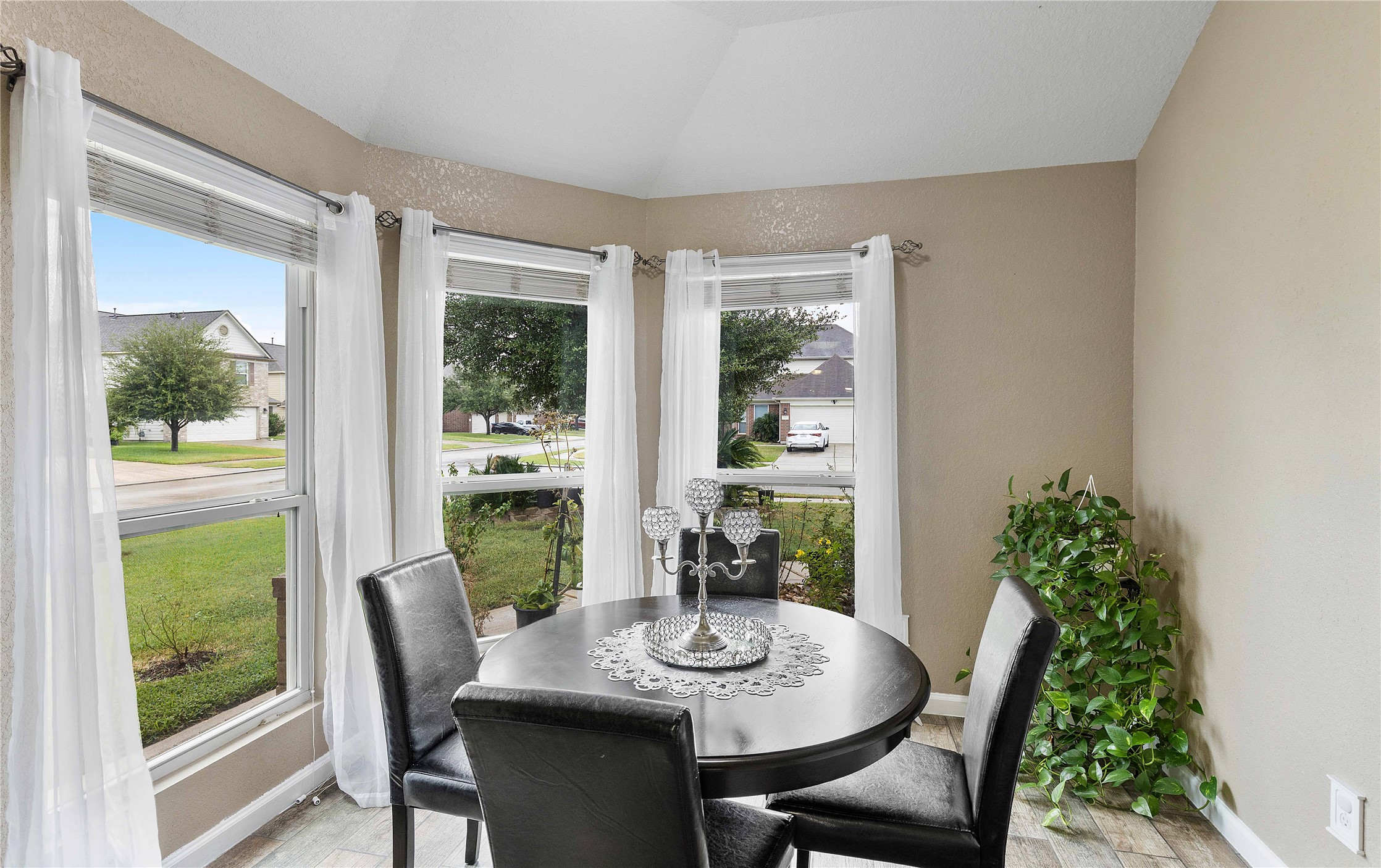 11031 Bauer Elm Street Houston, TX 77044 - Photo 7 of 33 Bright dining nook with large windows offering a view of the neighborhood. Features a round table, black chairs, and is accented by white curtains and a potted plant.