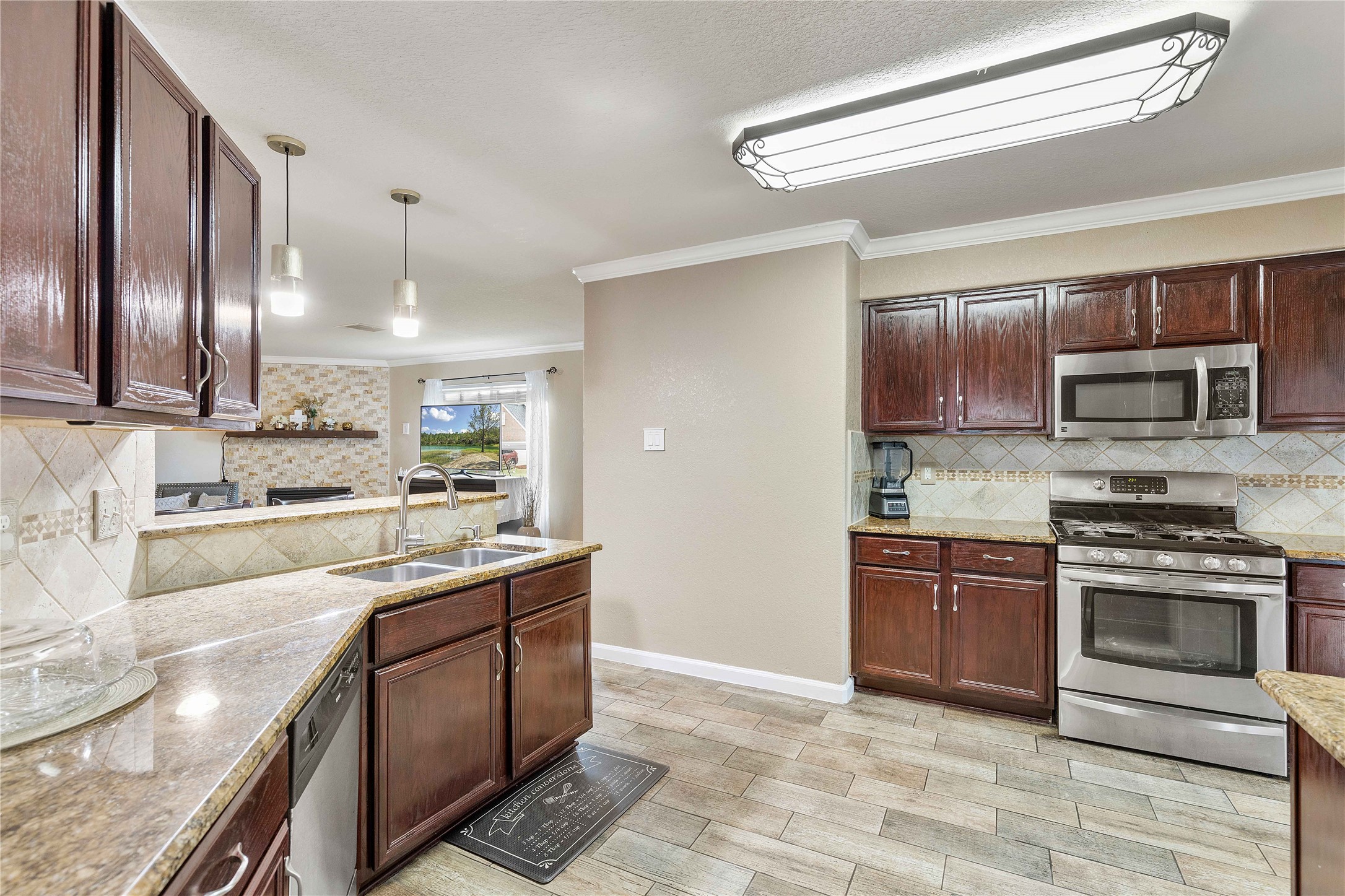 11031 Bauer Elm Street Houston, TX 77044 - Photo 10 of 33 This kitchen features elegant dark wood cabinets, stainless steel appliances, and granite countertops. It opens to the living area with a breakfast bar, pendant lighting, and a cozy atmosphere.