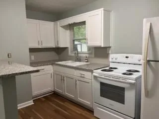 a kitchen with a stove white cabinetry a sink and a window