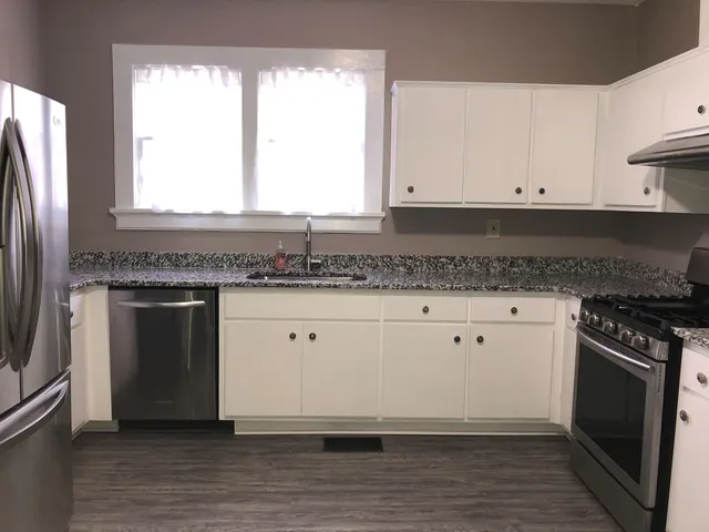 a kitchen with granite countertop white cabinets stainless steel appliances a sink and a window