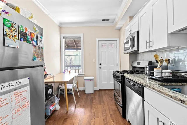 a kitchen with stainless steel appliances granite countertop a stove top oven a sink a dining table and chairs with wooden floor