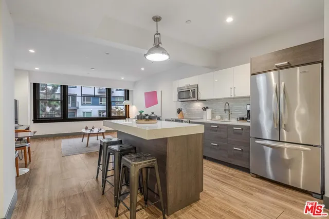 a kitchen with stainless steel appliances granite countertop a refrigerator a sink dishwasher a stove and a dining table with wooden floor