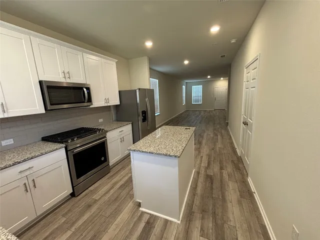 a kitchen with granite countertop a stove top oven a sink dishwasher and a refrigerator with wooden floor