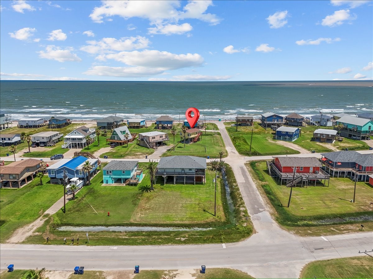 819 Seashell Drive Surfside Beach, TX 77541 - Photo 2 of 36 This aerial photo showcases a charming coastal neighborhood with colorful homes near the ocean. The property is marked with a pin, indicating its prime beachside location, offering stunning sea views and easy beach access. Perfect for those seeking a serene coastal lifestyle.
