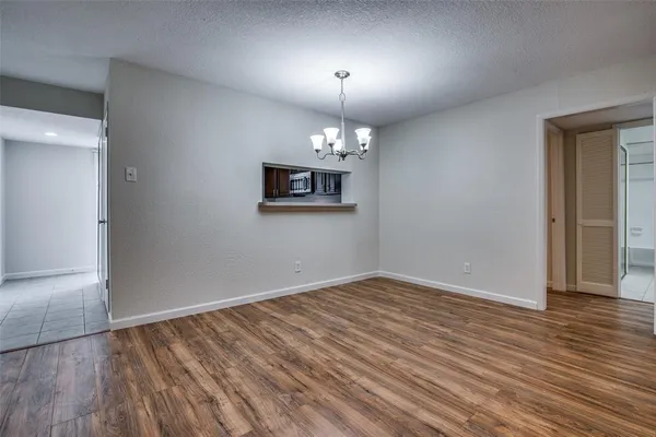 an empty room with wooden floor chandelier and windows