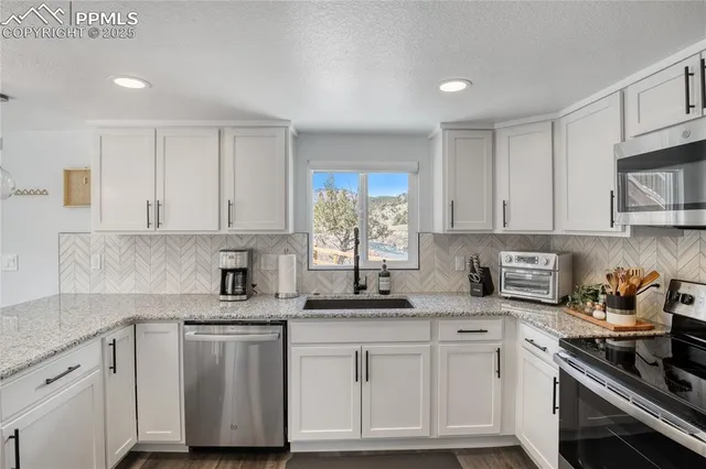 a kitchen with stainless steel appliances granite countertop white cabinets sink and window