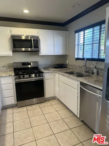 a white kitchen with granite countertop a stove top oven microwave and cabinets