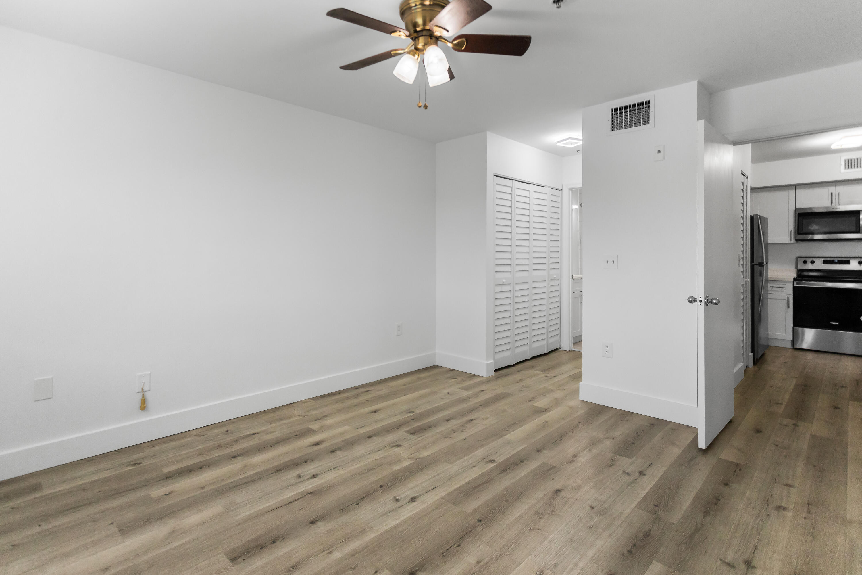 2113 Renaissance Boulevard, Unit 306 Miramar, FL 33025 - Photo 40 of 59 an empty room with wooden floor a ceiling fan and kitchen view