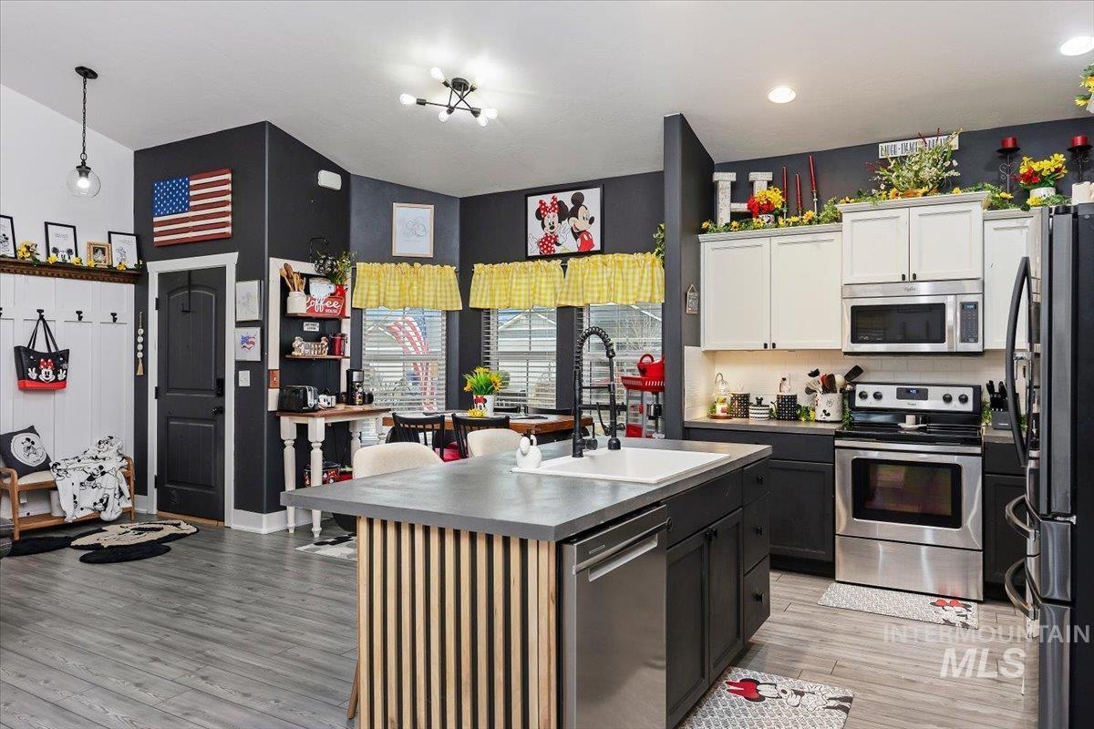389 Arrow Street Twin Falls, ID 83301 - Photo 11 of 34 Kitchen with stainless steel appliances, light wood-style floors, a kitchen island with sink, two tone cabinetry, and tasteful backsplash