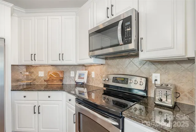 a kitchen with stainless steel appliances granite countertop white cabinets and a stove top oven