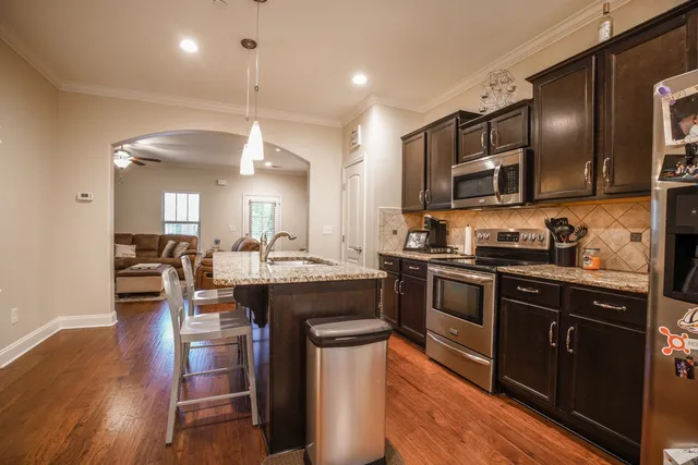 a kitchen with stainless steel appliances granite countertop a refrigerator a stove top oven a sink dishwasher and wooden floor