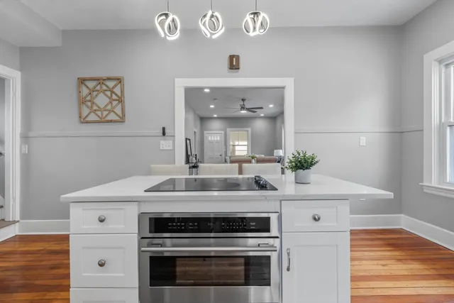 a kitchen with stainless steel appliances kitchen island granite countertop a stove a sink a refrigerator and white cabinets with wooden floor