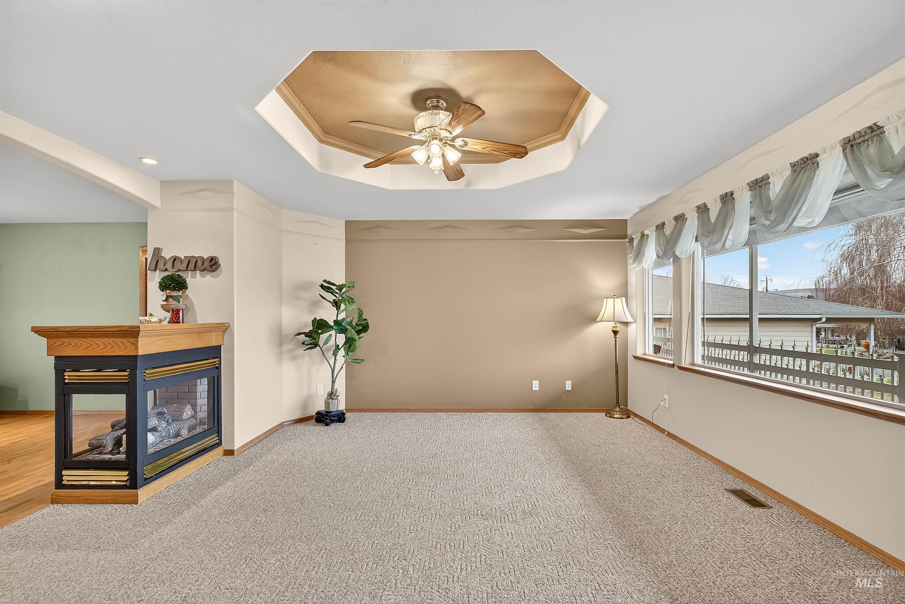 1324 Setlow Court Clarkston, WA 99403 - Photo 12 of 49 Carpeted empty room with a tray ceiling, a multi sided fireplace, and a ceiling fan