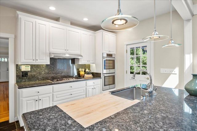 a kitchen with stainless steel appliances granite countertop a stove a sink and white cabinets with wooden floor