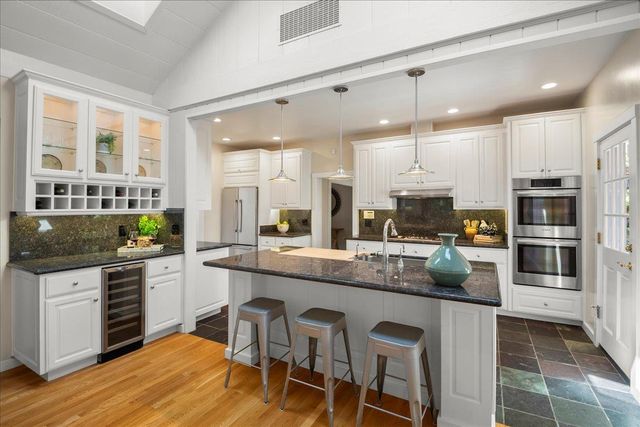 a kitchen with stainless steel appliances granite countertop a stove top oven a sink a dining table and chairs with wooden floor