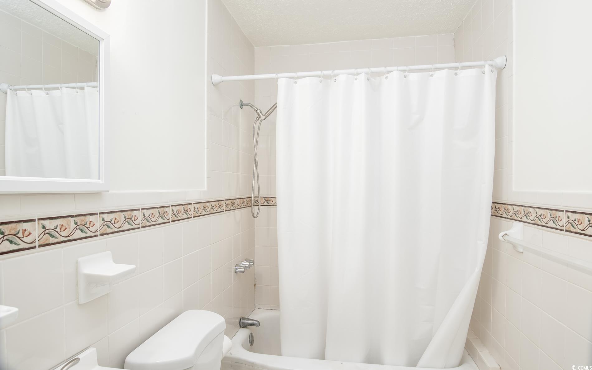 1019 Prince Street Georgetown, SC 29440 - Photo 20 of 20 Bathroom featuring tile walls, toilet, shower / bathtub combination with curtain, and wainscoting