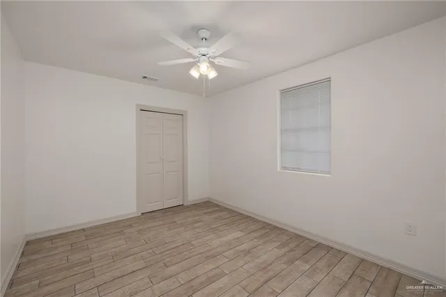 a view of an empty room with wooden floor and a fan