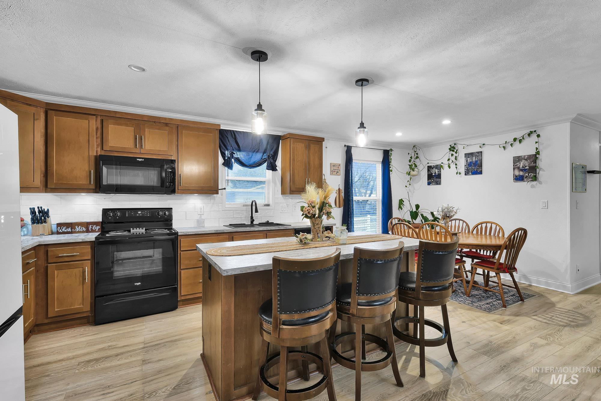 8483 West Irving Lane Boise, ID 83704 - Photo 5 of 40 Kitchen with black appliances, brown cabinets, a breakfast bar area, decorative backsplash, and ornamental molding