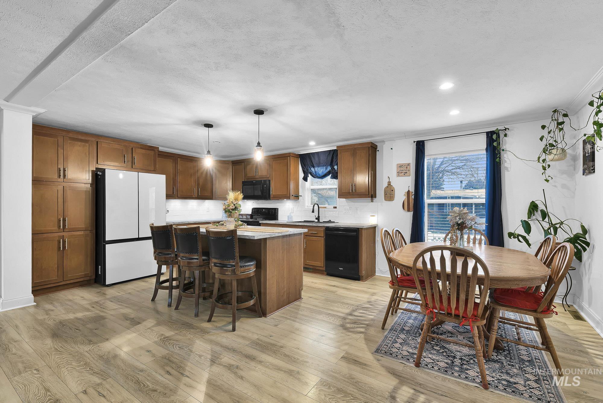 8483 West Irving Lane Boise, ID 83704 - Photo 6 of 40 Kitchen featuring a kitchen island, brown cabinets, decorative backsplash, black appliances, and a kitchen bar