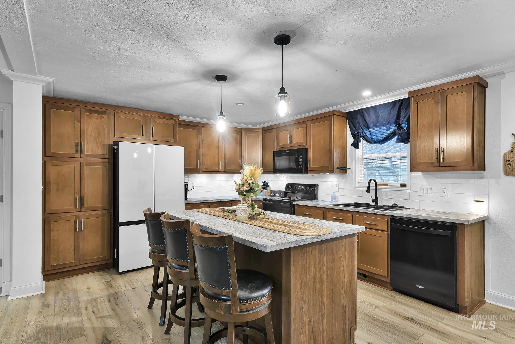 8483 West Irving Lane Boise, ID 83704 - Photo 8 of 40 Kitchen with brown cabinetry, black appliances, a center island, decorative light fixtures, and a kitchen breakfast bar