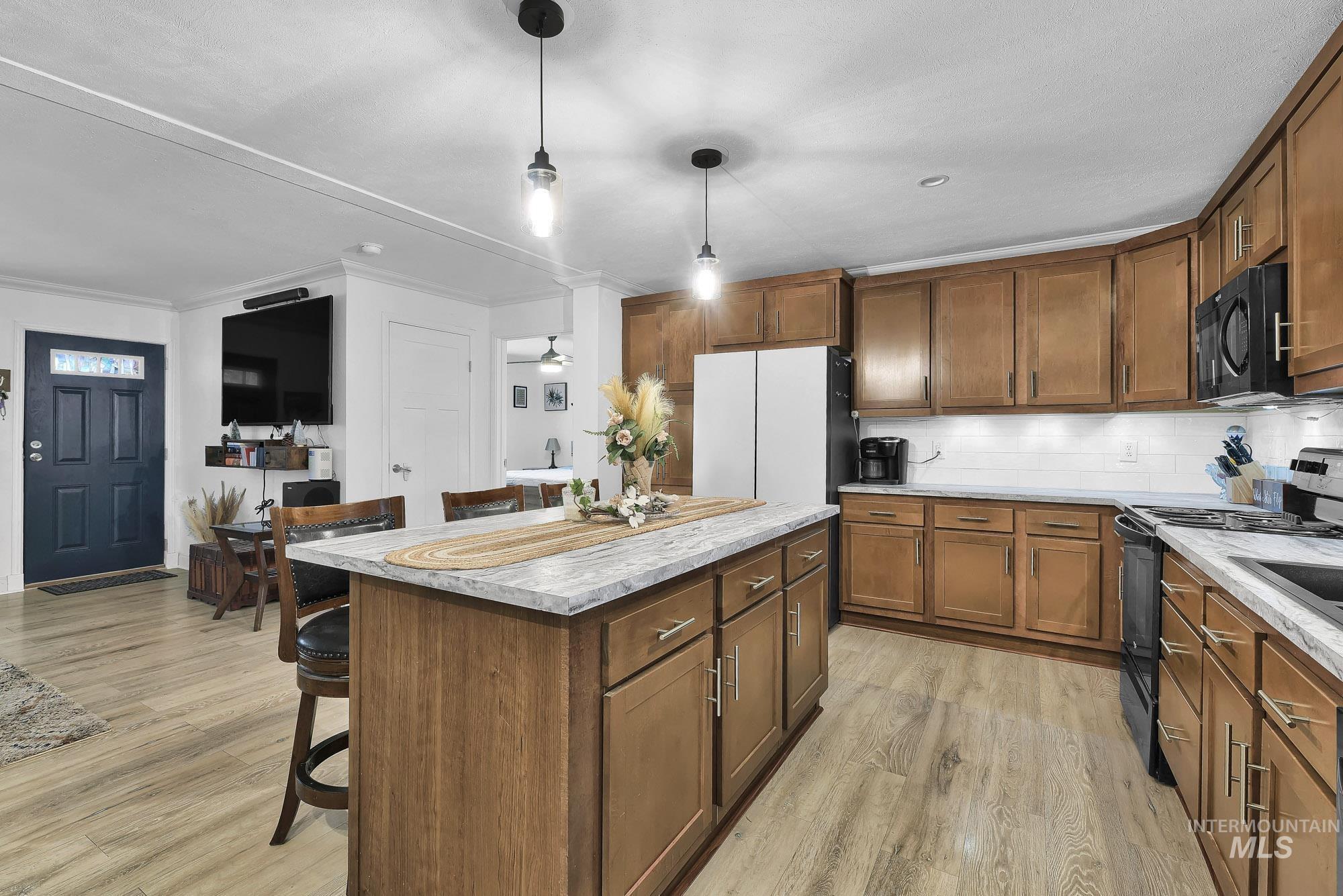 8483 West Irving Lane Boise, ID 83704 - Photo 9 of 40 Kitchen with a breakfast bar, black appliances, brown cabinetry, a kitchen island, and ornamental molding