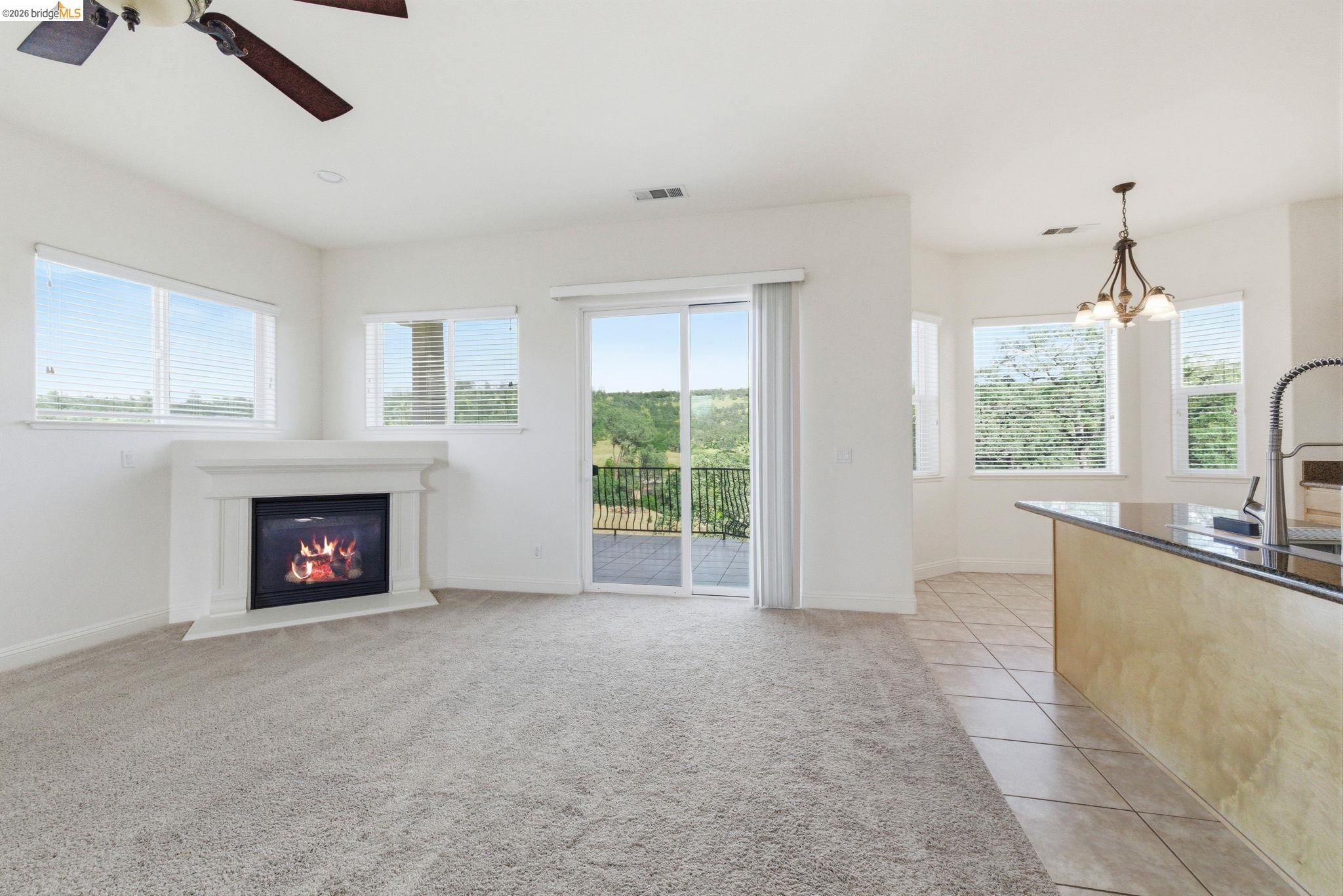 32 Apollo Lane Copperopolis, CA 95228 - Photo 12 of 58 Unfurnished living room with a ceiling fan, light tile patterned floors, a glass covered fireplace, light colored carpet, and hanging lights