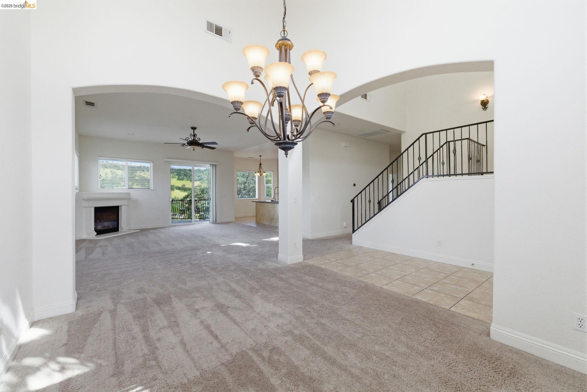 32 Apollo Lane Copperopolis, CA 95228 - Photo 9 of 58 Unfurnished living room with light carpet, arched walkways, a ceiling fan, a chandelier, and a fireplace with raised hearth