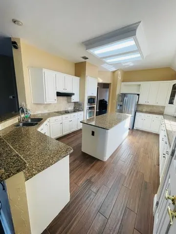 a living room with stainless steel appliances kitchen island granite countertop wooden floor and a sink