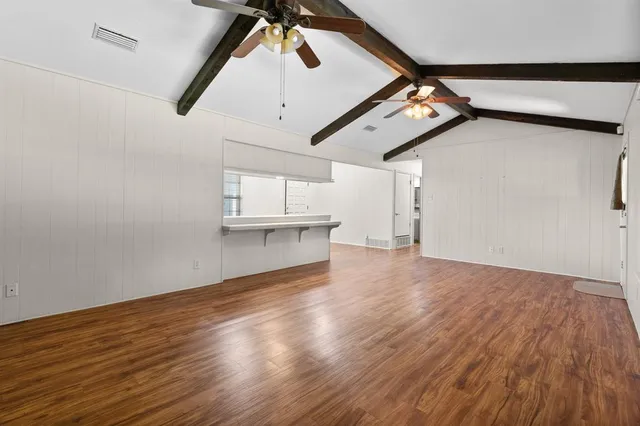 a view of an empty room with wooden floor and a ceiling fan