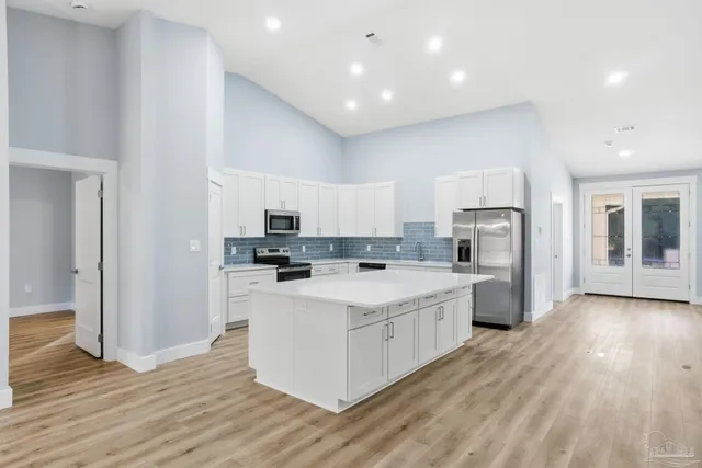 a large kitchen with stainless steel appliances granite countertop a stove a sink a refrigerator and white cabinets with wooden floor