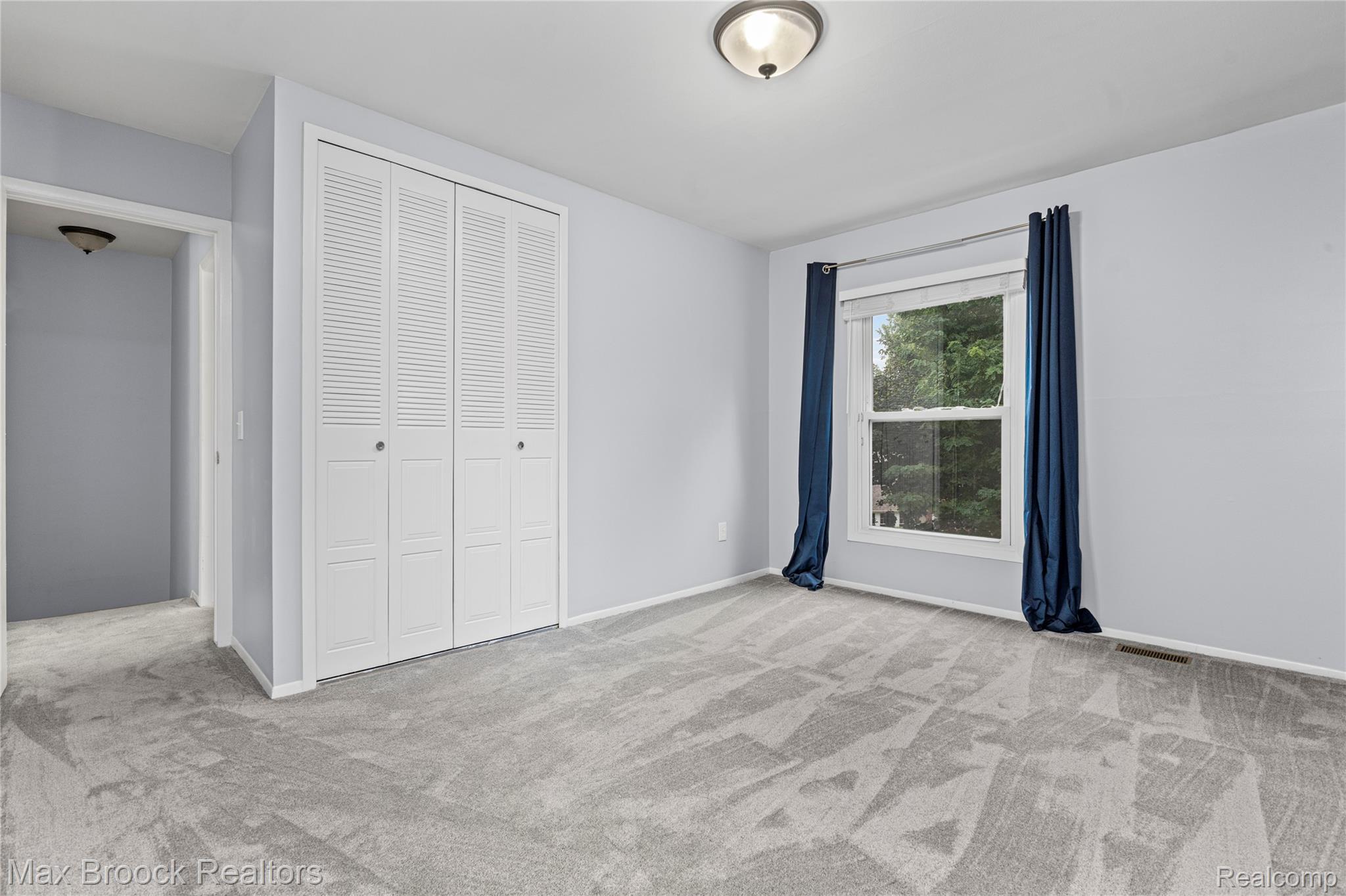 1157 Pine Ridge Court Rochester, MI 48306 - Photo 27 of 55 Spacious bedroom with engineered wood-finish flooring featuring geometric patterning, abundant natural light from dual windows with blue drapery, white louvered closet doors with dual panels, and neutral wall finishes throughout
